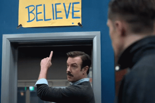 Ted Lasso pointing to a sign that says - Believe